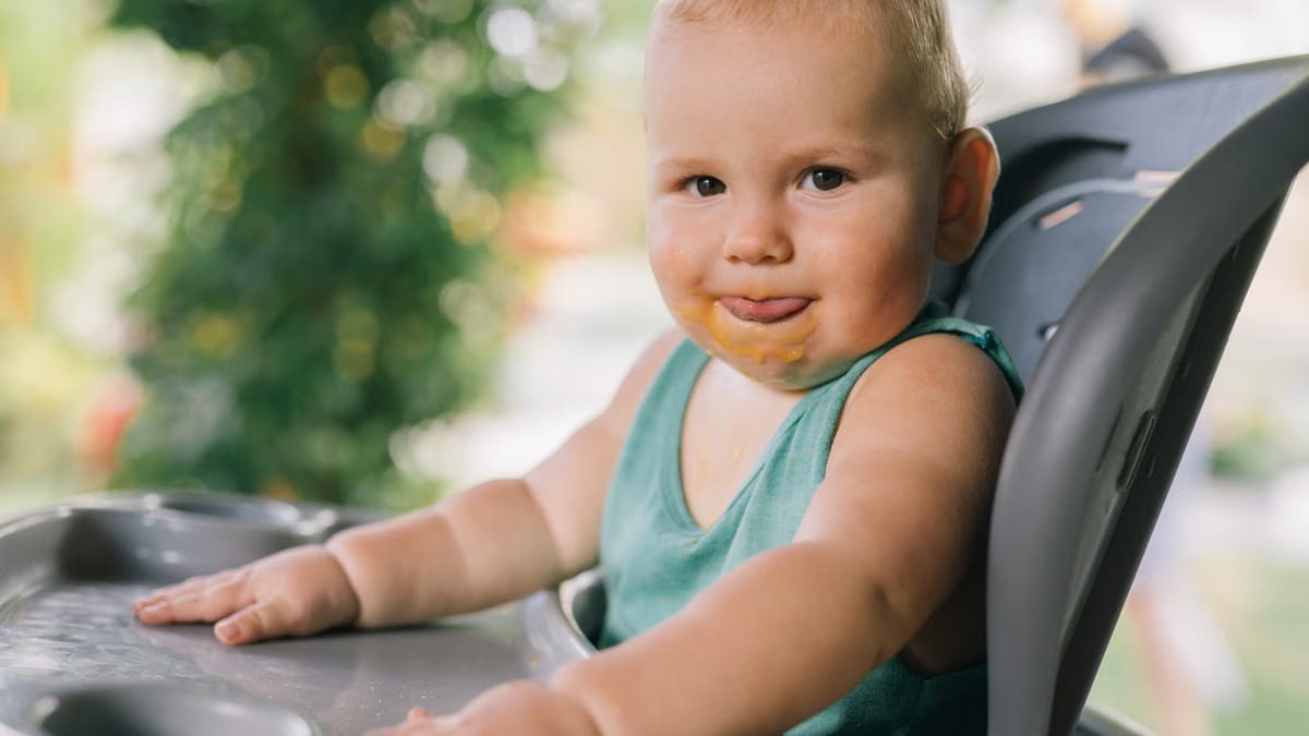Charming toddler eating in a high chair outside, enjoying a sunny day.