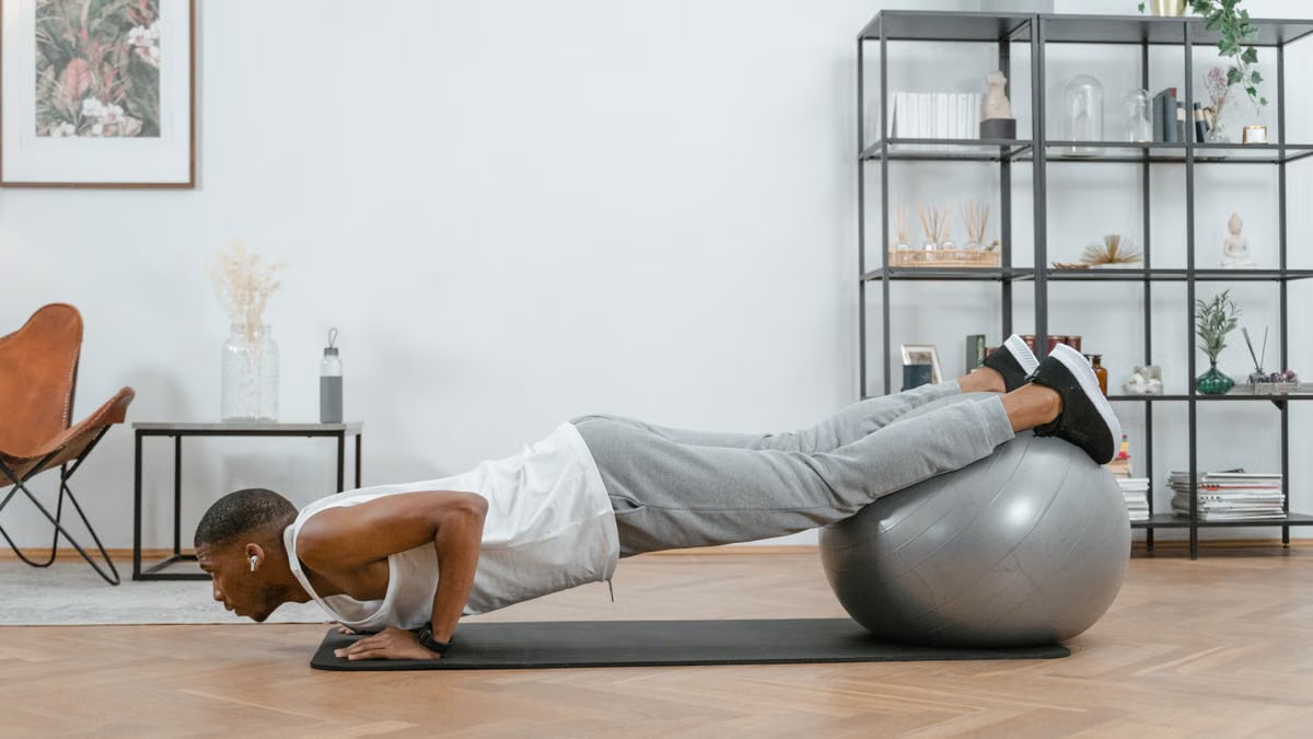 Adult doing push-ups with an exercise ball indoors for fitness and health.